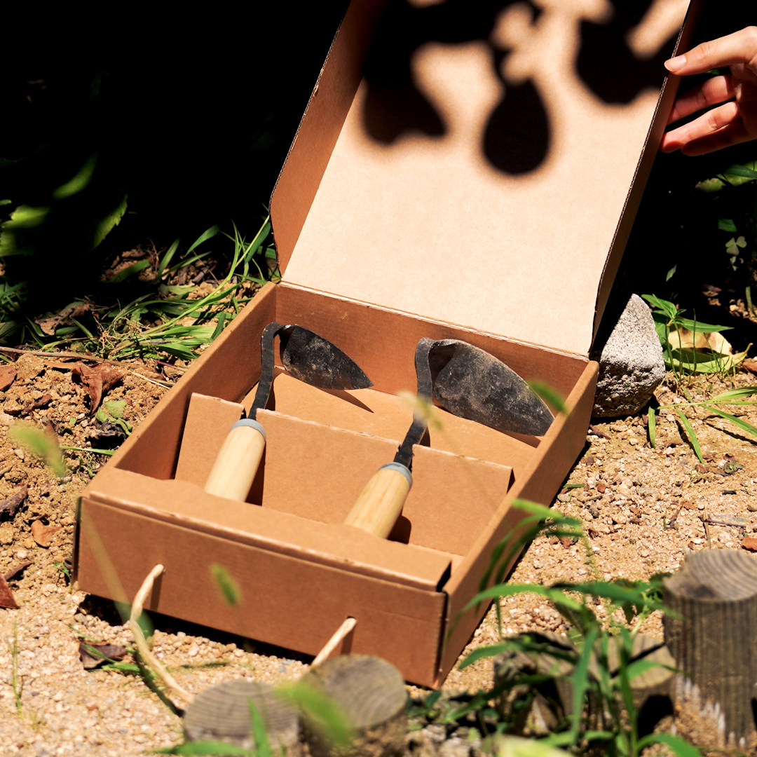 Three garden tools in a cardboard box on a natural outdoor background